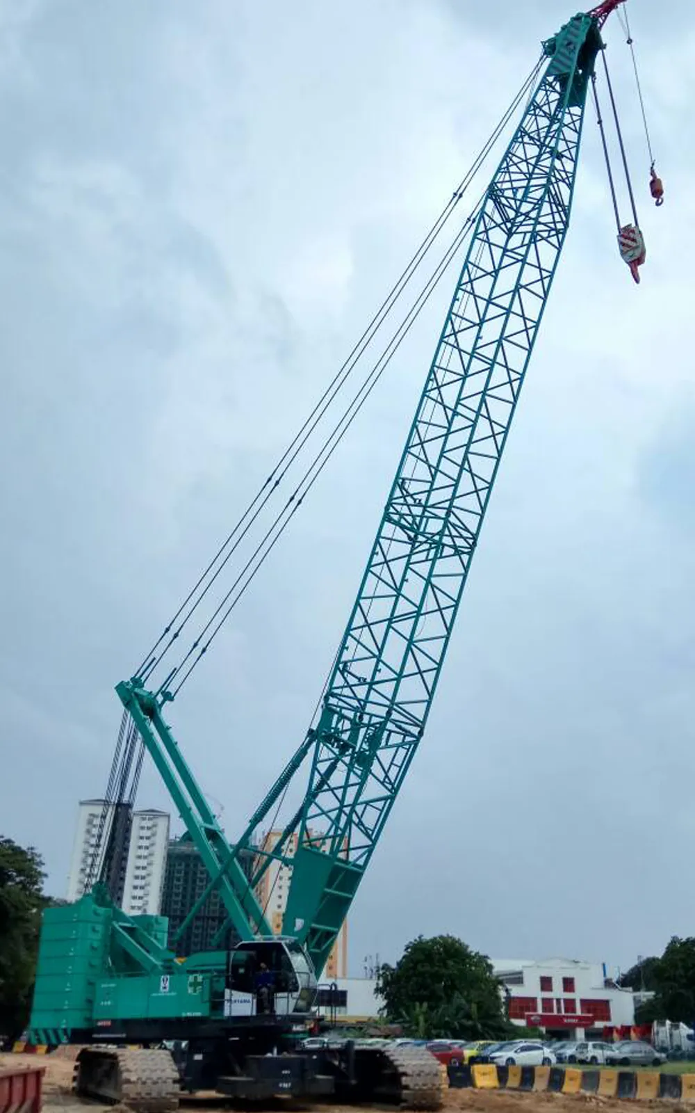 Green Kobelco crawler crane with fly jib raised against a cloudy sky