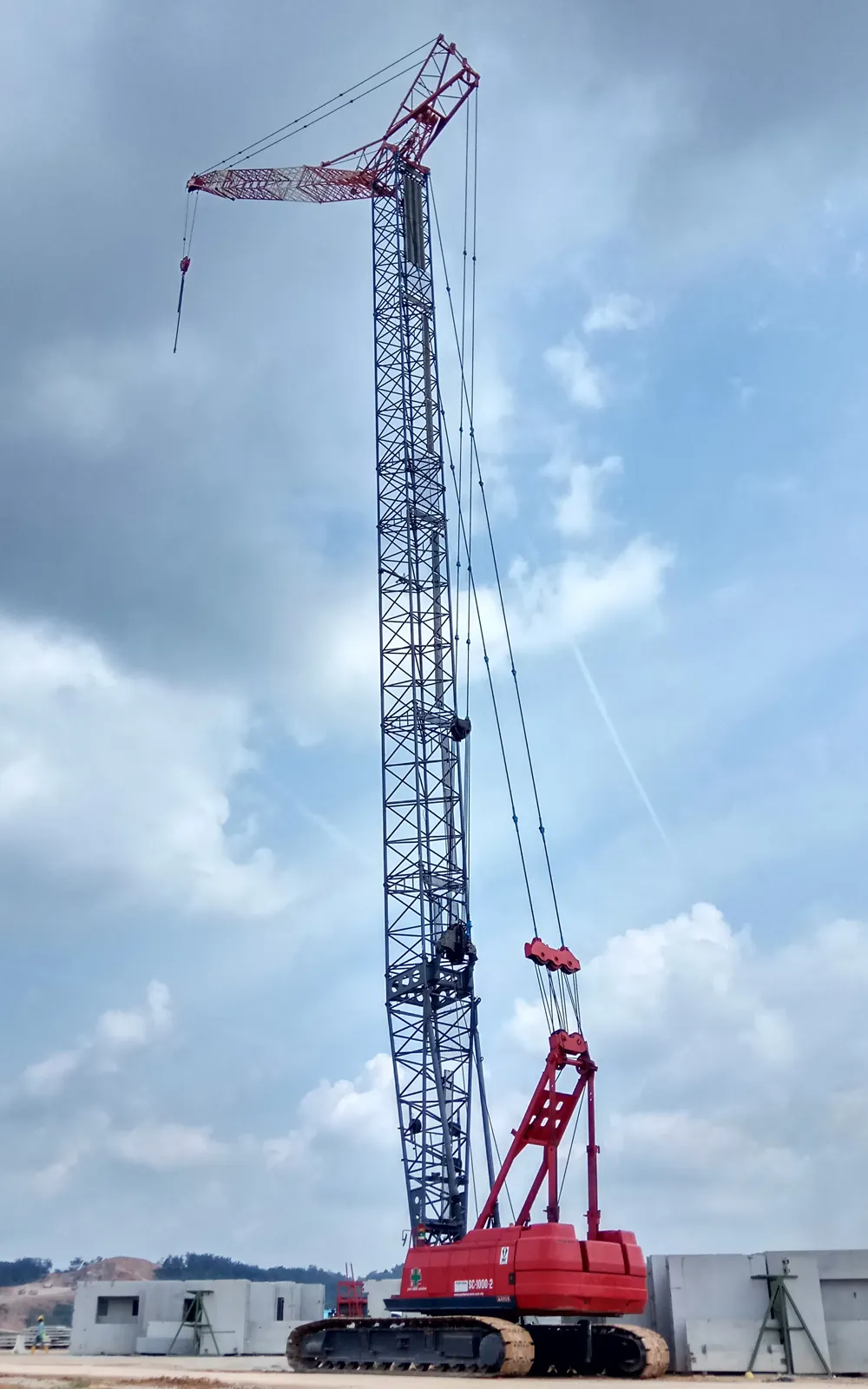 Red and white crawler tower crane with luffing jib at full height on site
