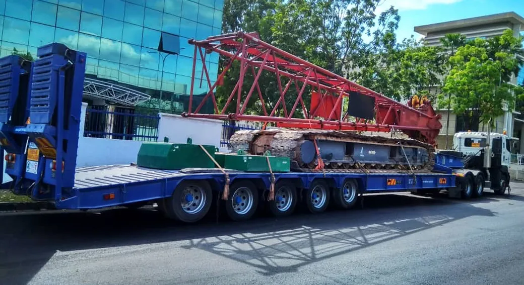 Hino 5-axle low loader trailer transporting a red crawler crane boom section