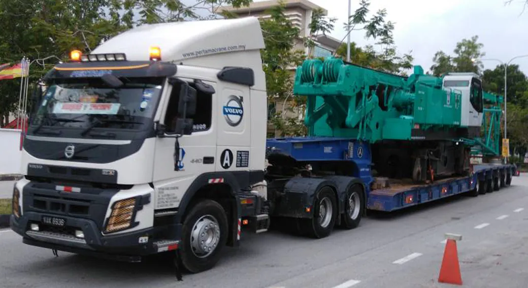White Volvo prime mover with 6-axle low loader carrying a green crawler crane